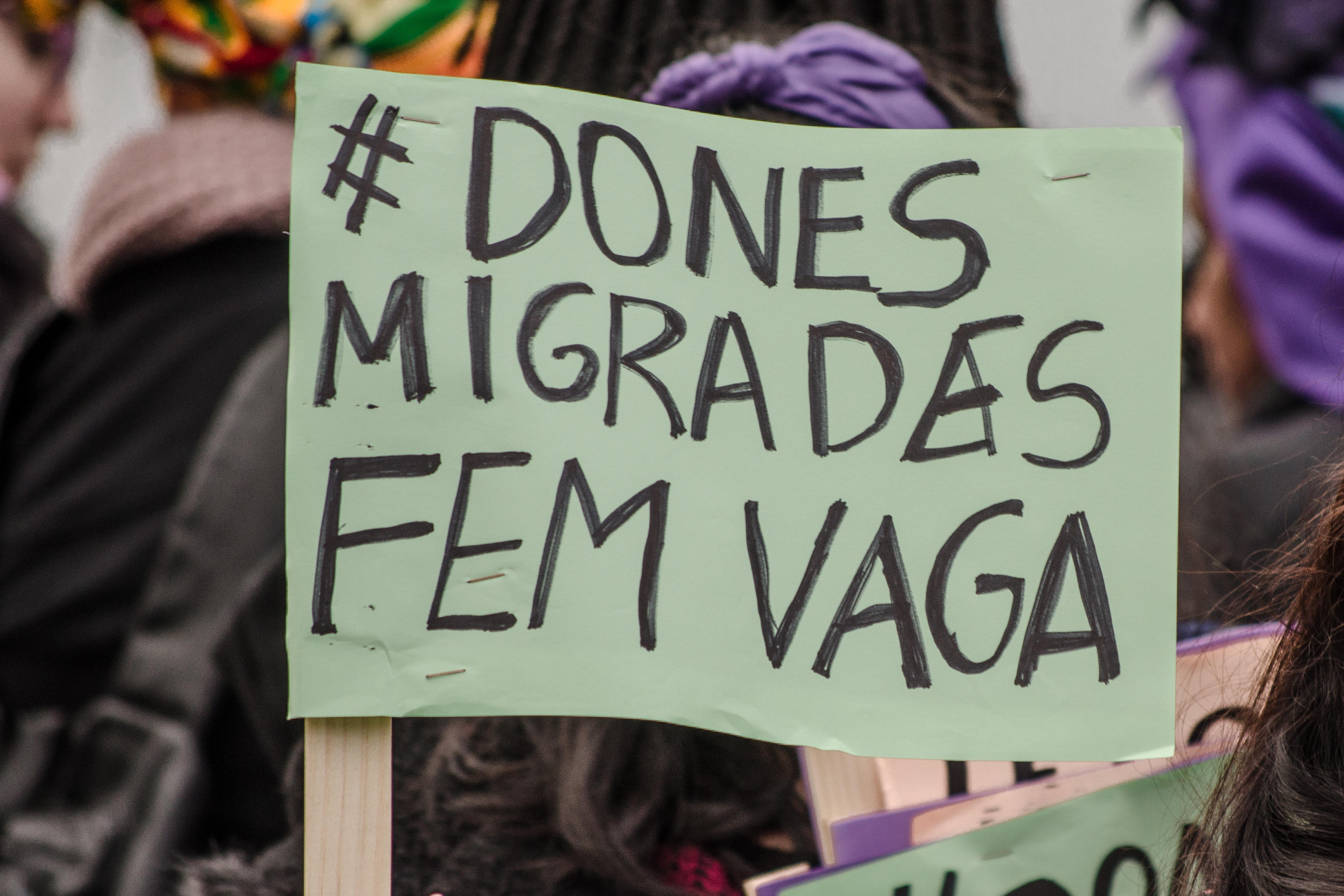 A protester seen displaying a poster relating to migrant women on strike. The Poster says 'Dones Migrades Fem vaga', 'Migrant women on the move'.