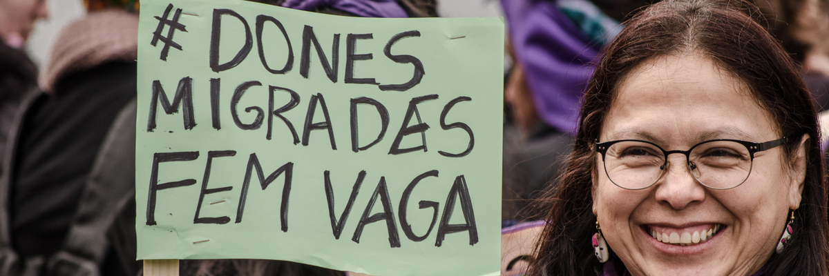 A protester seen displaying a poster relating to migrant women on strike. The Poster says 'Dones Migrades Fem vaga', 'Migrant women on the move'.