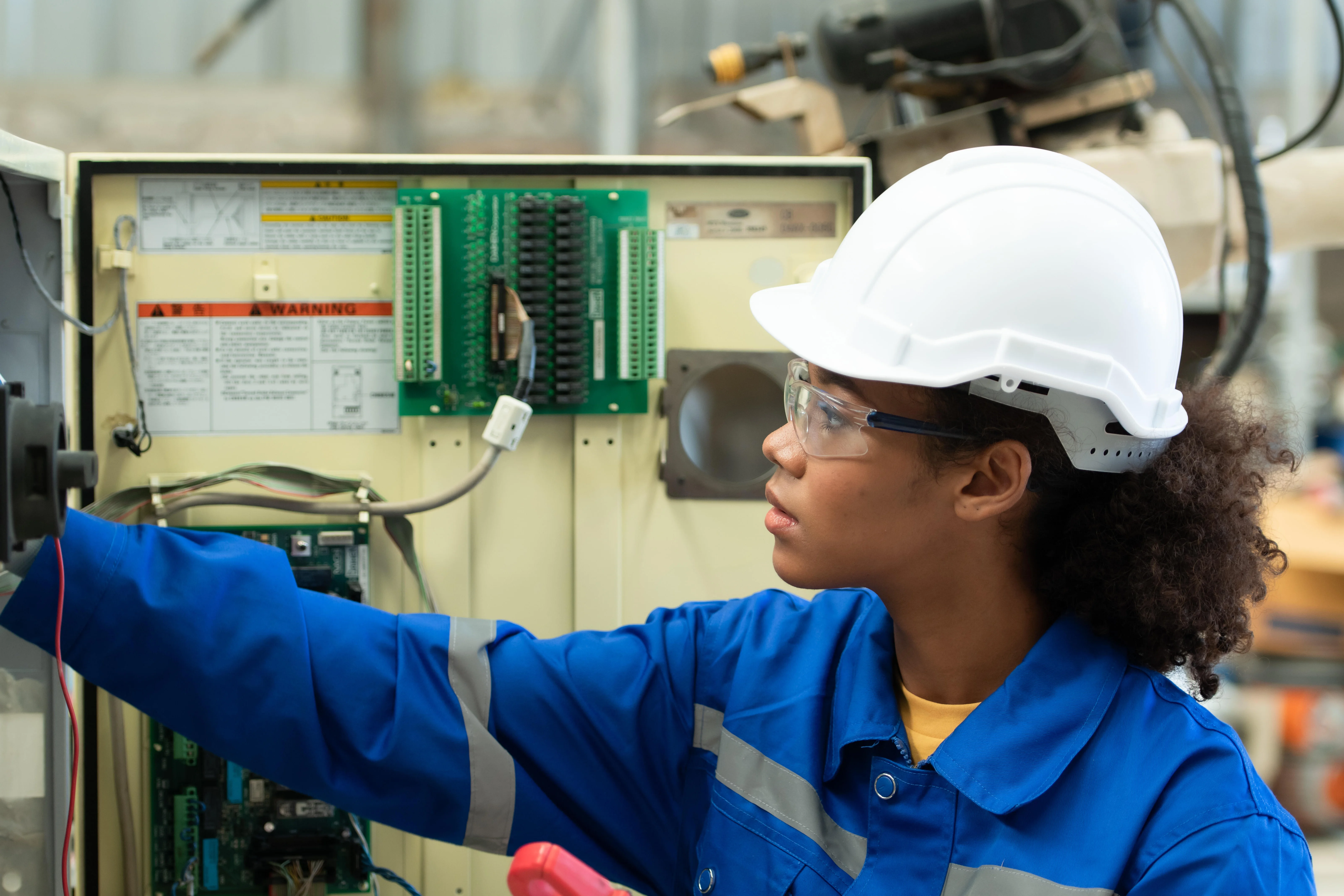 Eine junge Elektroingenieurin überprüft das elektrische Steuerungssystem des Schweißroboters und testet dessen Funktionsfähigkeit.