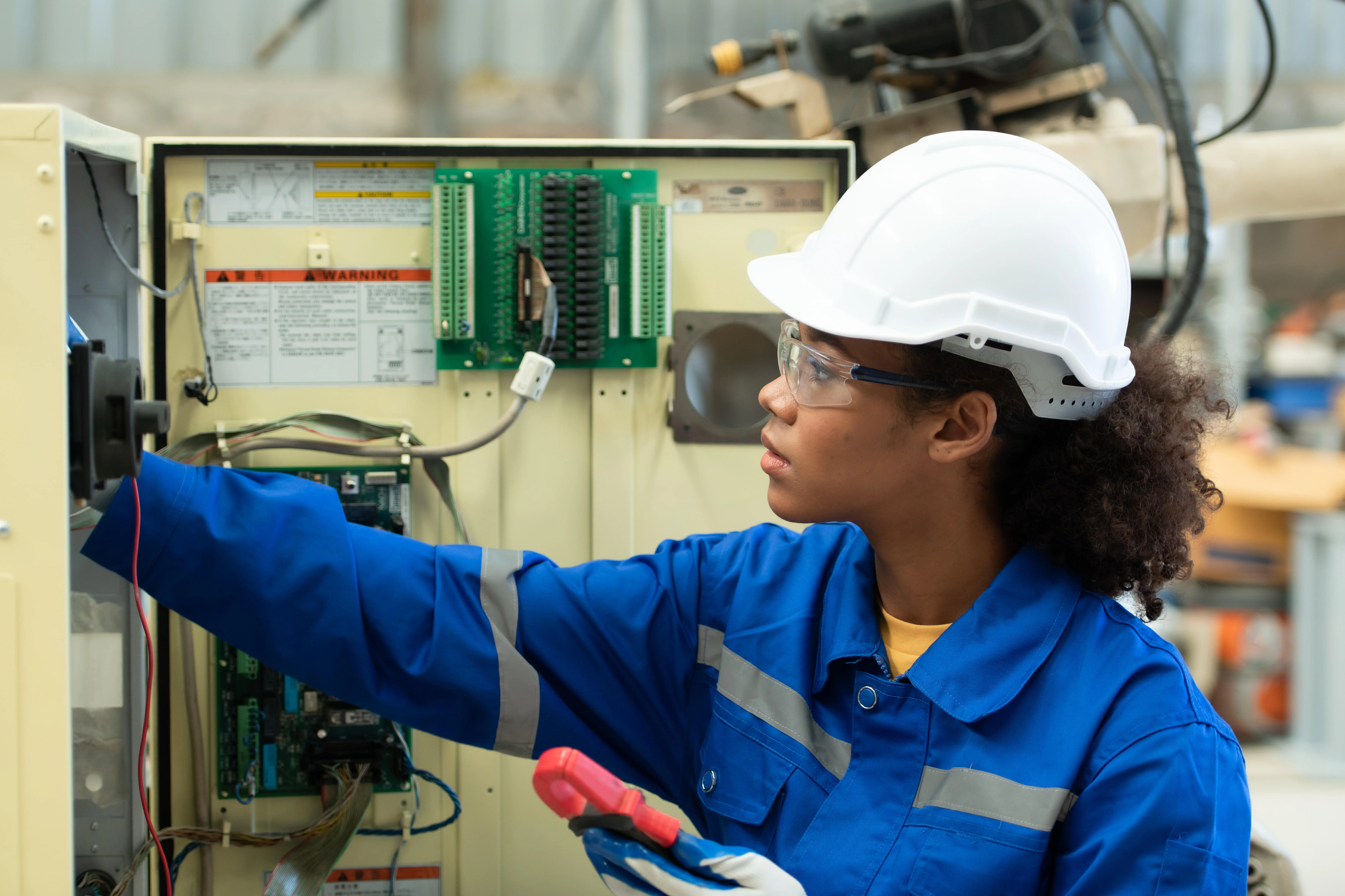 Eine junge Elektroingenieurin überprüft das elektrische Steuerungssystem des Schweißroboters und testet dessen Funktionsfähigkeit.