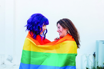 Zwei frauen blicken einander lachend in die Augen und umhüllen sich mit einer Regenbogenflagge.