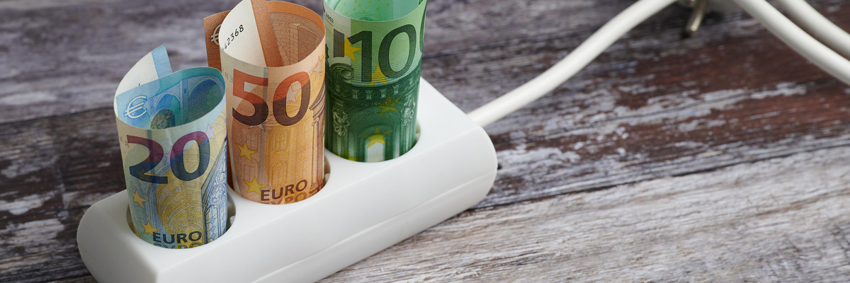 Foto von einer Dreiersteckdose, in der drei zusammengerollte Geldscheine stecken.