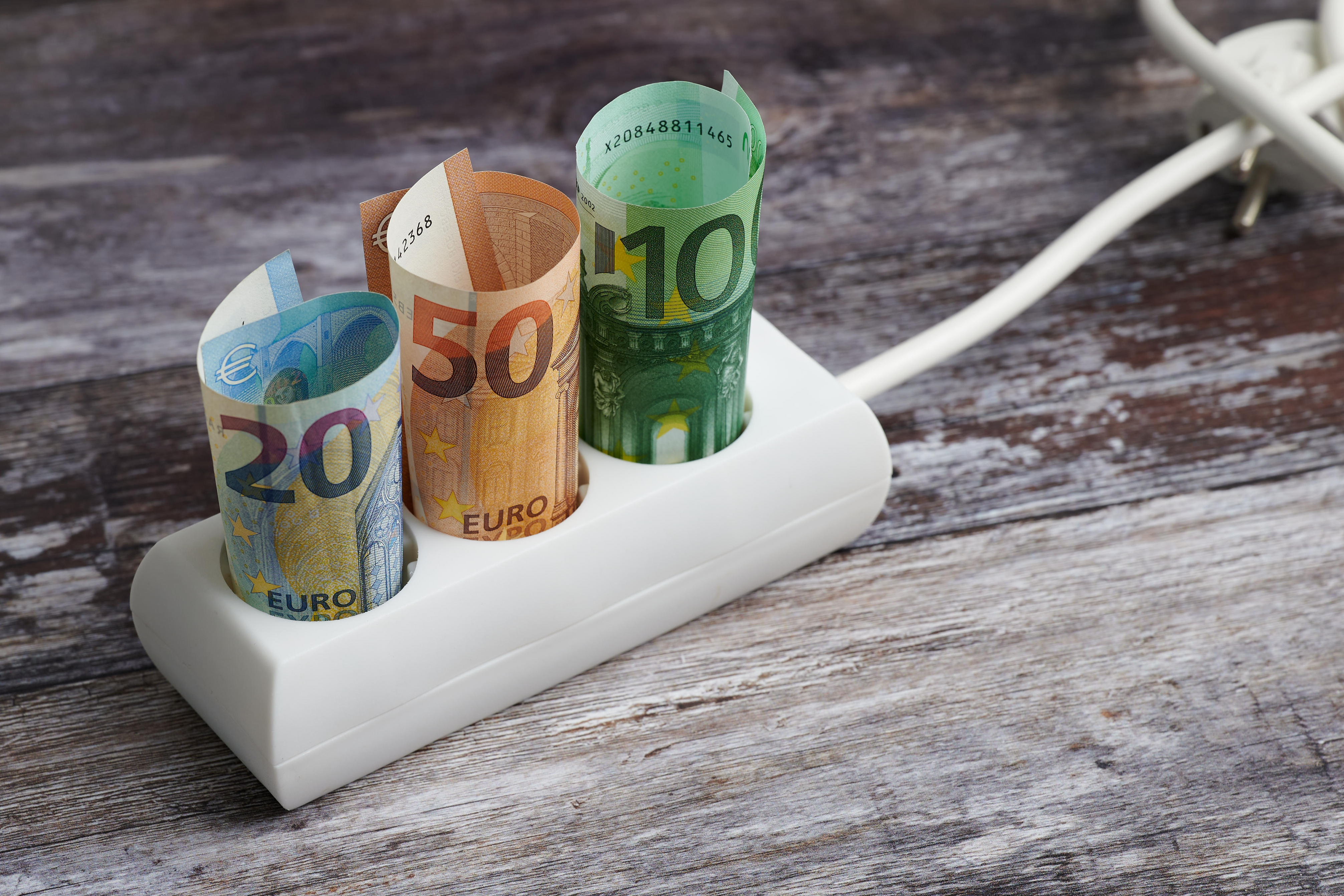 Foto von einer Dreiersteckdose, in der drei zusammengerollte Geldscheine stecken.