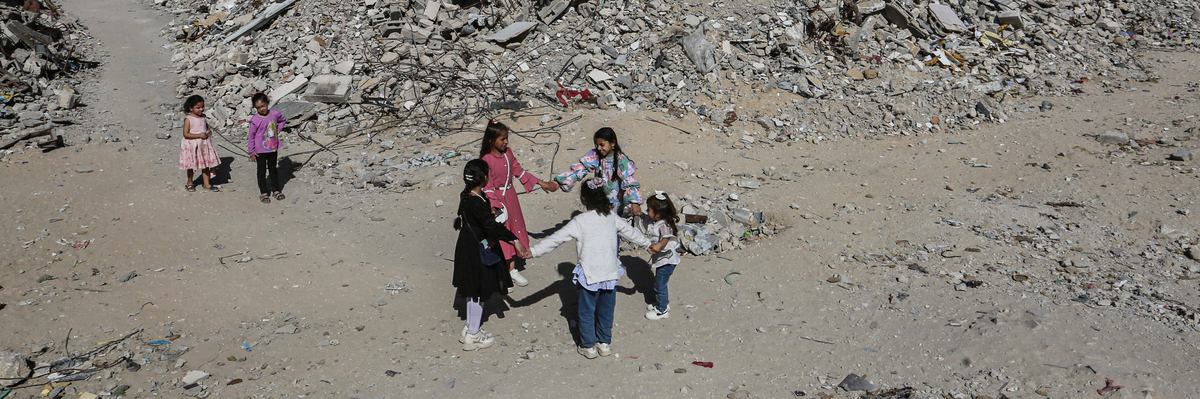 Mädchen tanzen Hand in Hand inmitten der Trümmer von Gebäuden und provisorischen Zelten