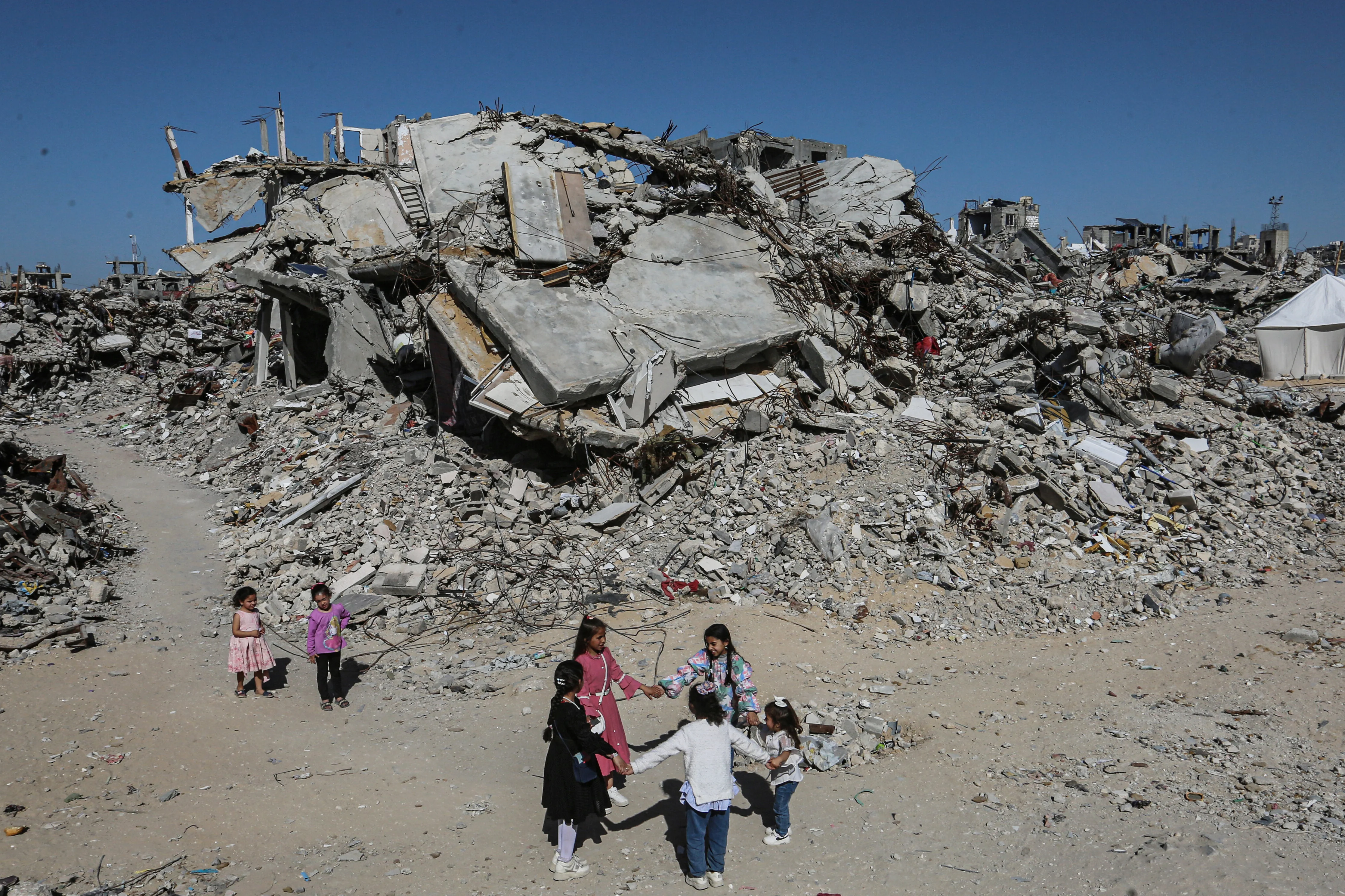 Mädchen tanzen Hand in Hand inmitten der Trümmer von Gebäuden und provisorischen Zelten