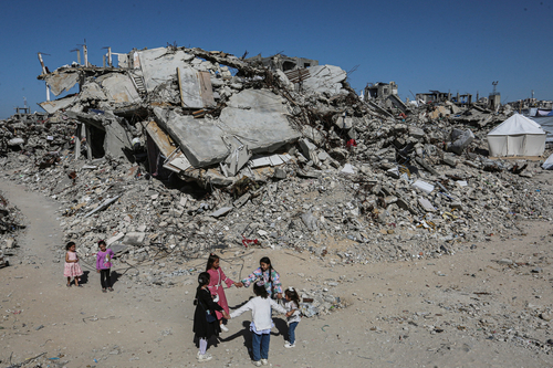 Mädchen tanzen Hand in Hand inmitten der Trümmer von Gebäuden und provisorischen Zelten