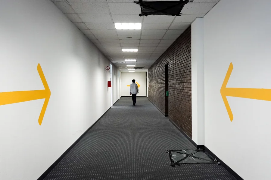 Ein Mitarbeiter geht durch einen Gang im Landesamt für Flüchtlingsangelegenheiten. Gelbe Pfeile an den Wänden zeigen in Richtung des Flures.