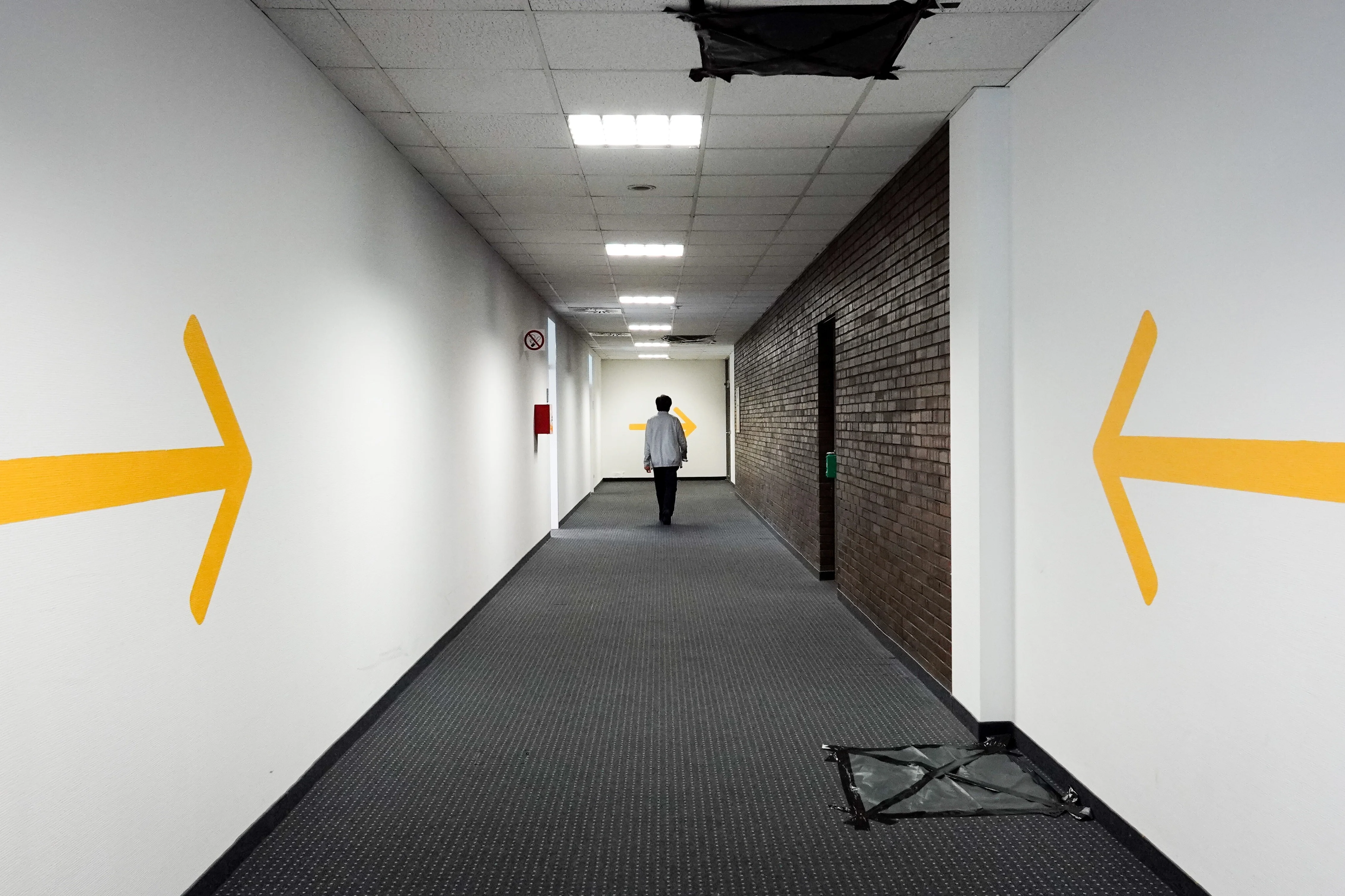 Ein Mitarbeiter geht durch einen Gang im Landesamt für Flüchtlingsangelegenheiten. Gelbe Pfeile an den Wänden zeigen in Richtung des Flures.
