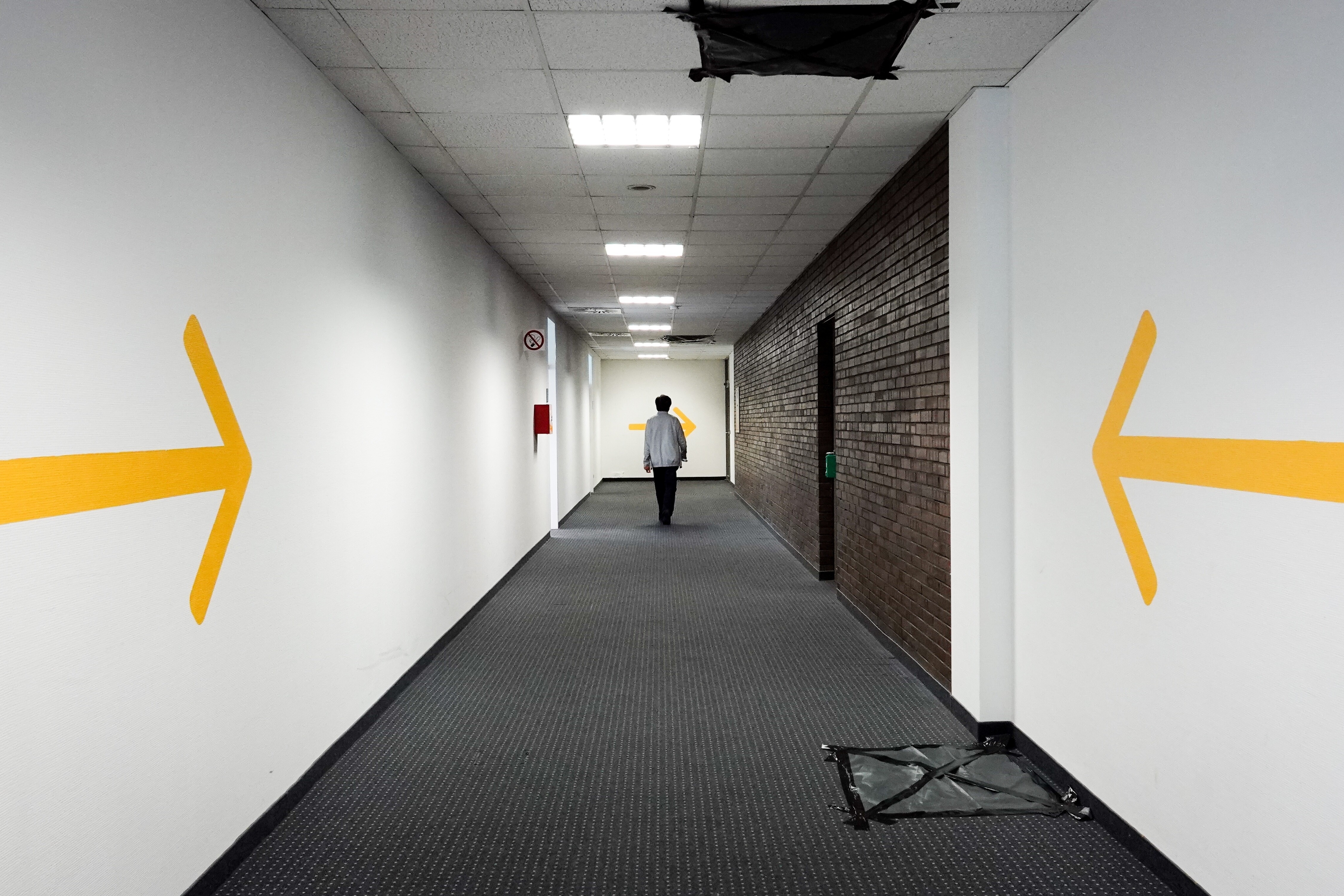 Ein Mitarbeiter geht durch einen Gang im Landesamt für Flüchtlingsangelegenheiten. Gelbe Pfeile an den Wänden zeigen in Richtung des Flures.