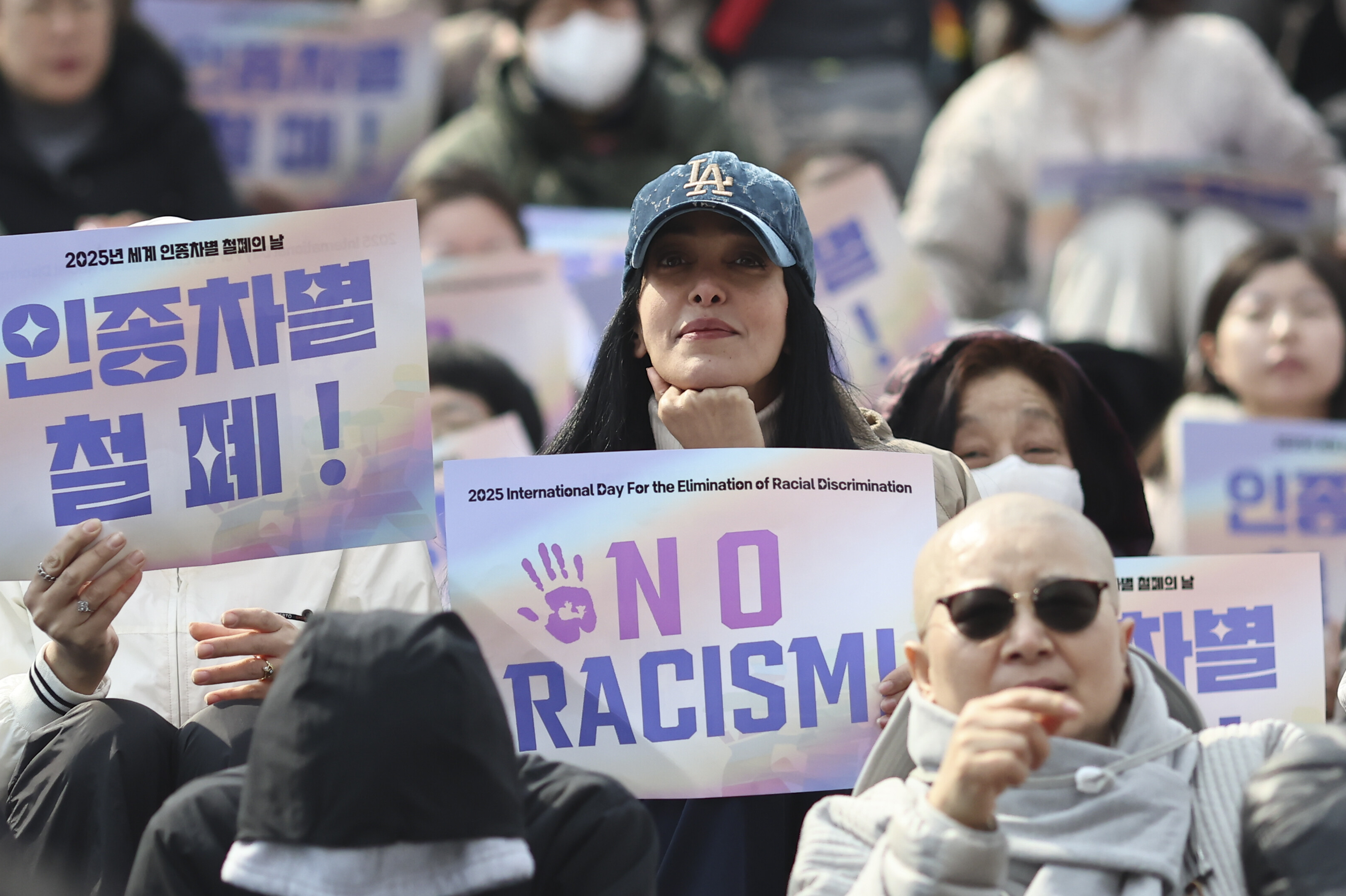 Demonstrant_innen halten ein Schild mit der Aufschrift "No racism" während einer Demonstration gegen Rassismus.