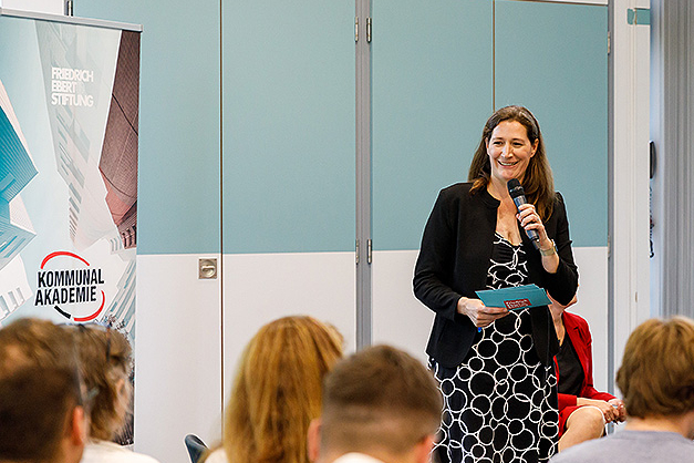 Seminarsituation. Referentin vorne neben Banner der Kommunalakademie. 