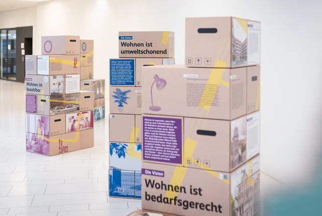 Ansicht der Wohnen-Ausstellung: Es sind mehrere Stapel aus bedruckten Umzugskartons zu sehen.