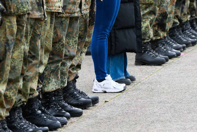 Eine Reihe Soldaten, daneben zwei Personen in zivil