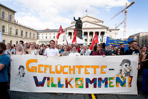 Protestierende Menschen halten ein Banner mit der Aufschrift "Geflüchtete Willkommen!"