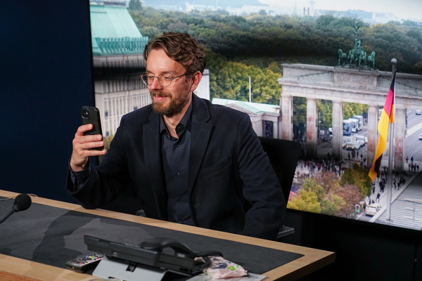 Foto: Ein junger Mann sitzt auf Position für die Live-Schalte aus dem ZDF-Hauptstadtstudio und macht ein Selfies vor dem Hintergrund des Brandenburger Tors.