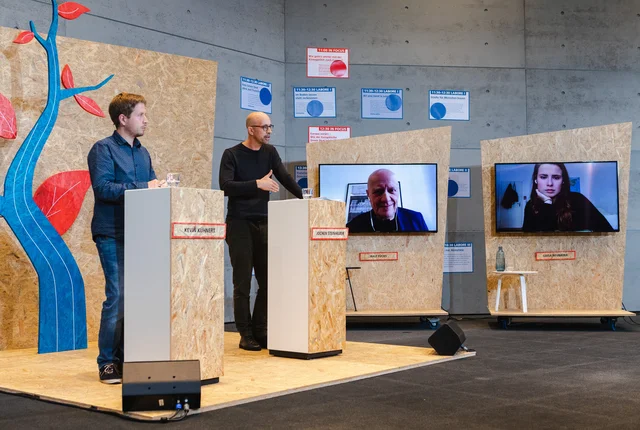 Jochen Steinhilber und Kevin Kühnert an Stehpulten im Studio bei der Aufzeichnung des Global Green Deals Forum 2020. Ralf Fücks und Luisa Neubauer sind auf Bildschirmen virtuell zugeschaltet. 