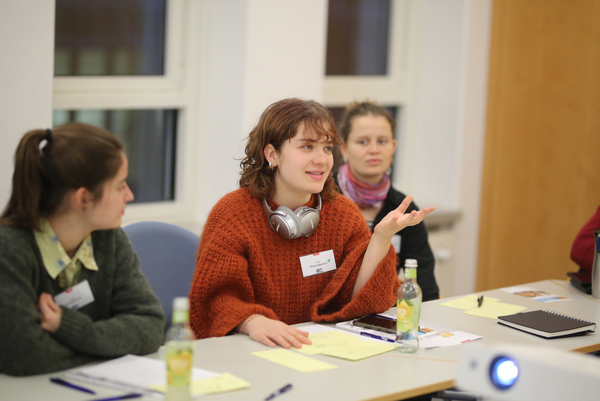 Eine junge Teilnehmerin sitzt in einem Seminar an einem Tisch und diskutiert.