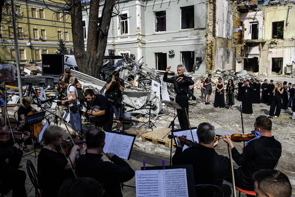 Ein Dirigent dirigiert ein Sinfonieorchester unter freiem Himmel vor den Ruinen einen Kinderkrankenhauses in Kiew. Das Haus ist von Bomben zerstört worden. 