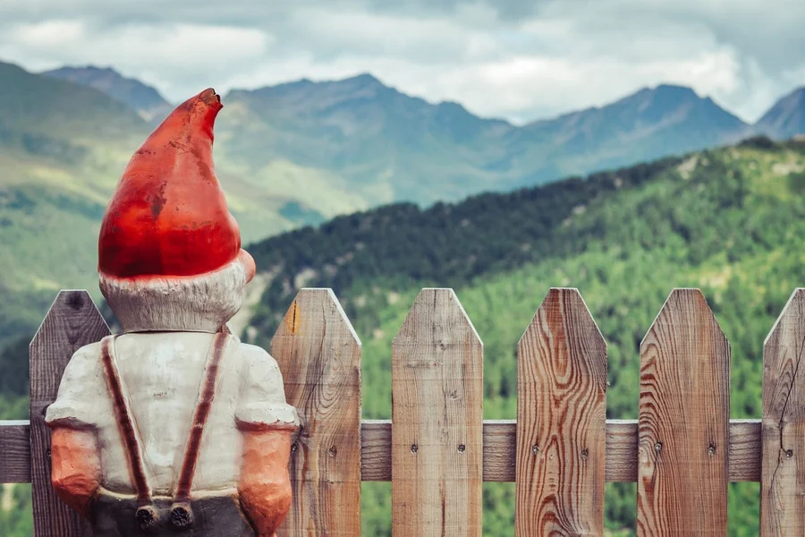 Ein am Zaun stehender Gartenzwerg blickt in die Ferne