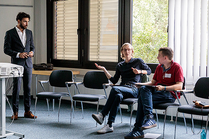 Seminarsituation: Trainer vorne und zwei diskutierende Teilnehmer im Plenum.