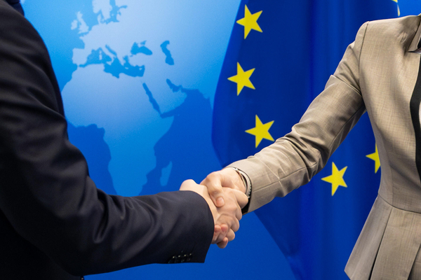 Handschlag vor Europaflagge und Grafik einer Weltkarte.