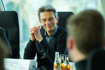 Rolf Mützenich sitzt am Tisch mit Teilnehmenden und hört ihnen zu.