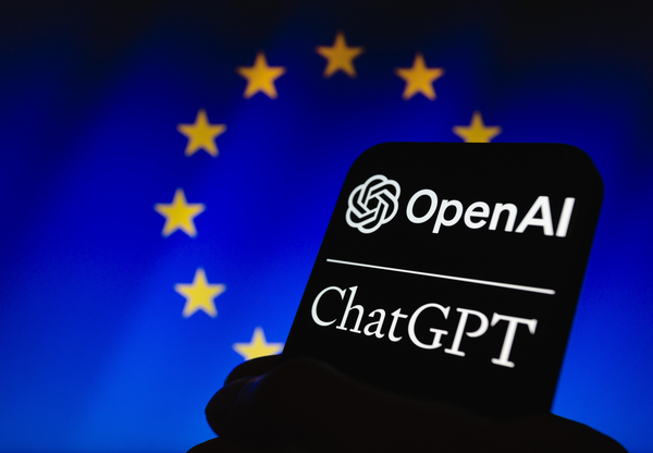  OpenAI Logo und der Name ''ChatGPT'' angezeigt auf einem Smartphone. Im Hintergrund eine Flagge der EU.