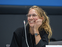 Eine Teilnehmerin sitzt, das Kinn auf die Hand gestützt, an einem Konferenztisch.