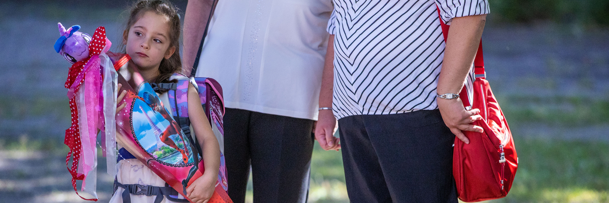 Ein kleines Mädchen mit Schultüte steht vor zwei erwachsenen Personen.