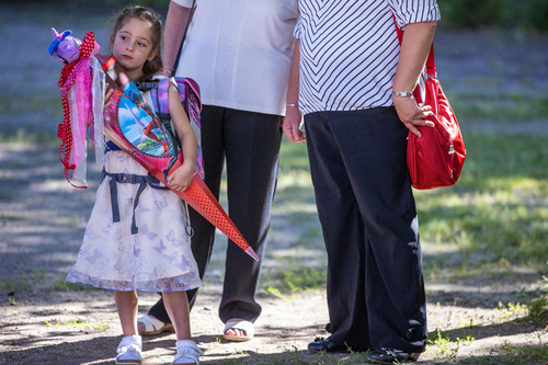 Ein kleines Mädchen mit Schultüte steht vor zwei erwachsenen Personen.