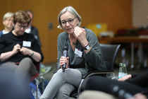Ulrike Schnellbach sitzt auf einem Seminar im Stuhlkreis, hält ein Mikrofon in der Hand und argumentiert.