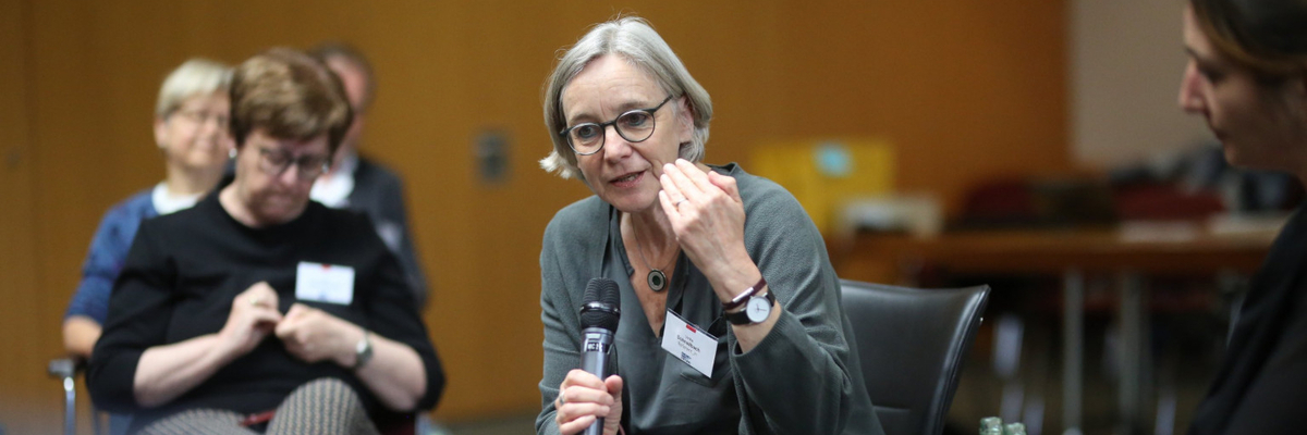 Ulrike Schnellbach sitzt auf einem Seminar im Stuhlkreis, hält ein Mikrofon in der Hand und argumentiert.