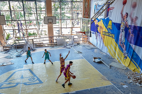 Jugendliche spielen in einer teilzerstörten Sporthalle in Kyiv Basketball.