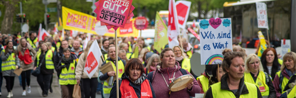 Menschen auf einer Demo von Verdi halten Schilder hoch mit Aufschriften wie "Wir sind es wert"