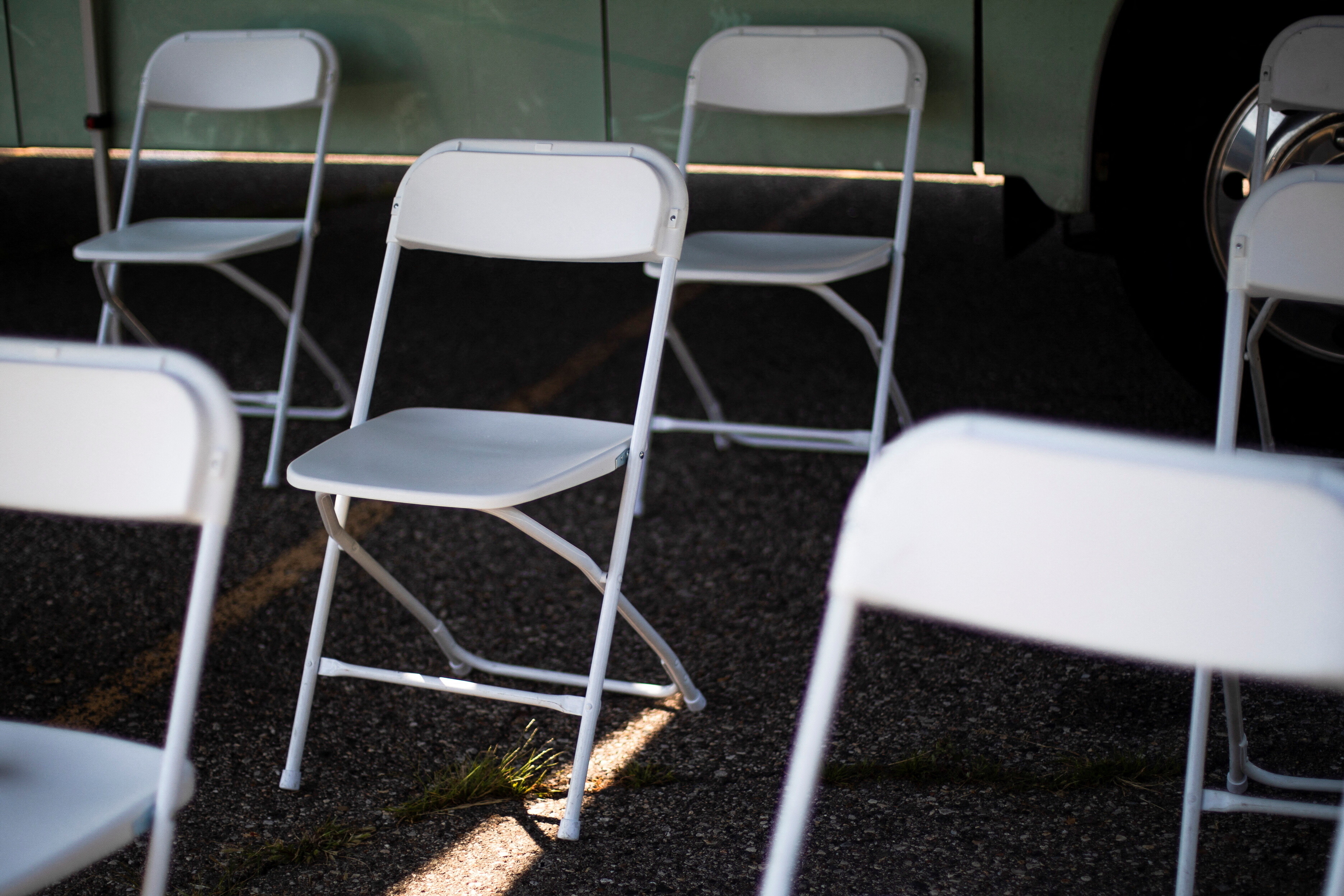 Leere weiße Klappstühle in einem Wartebereich. Ein Sonnenstrahl scheint auf den Fußboden.