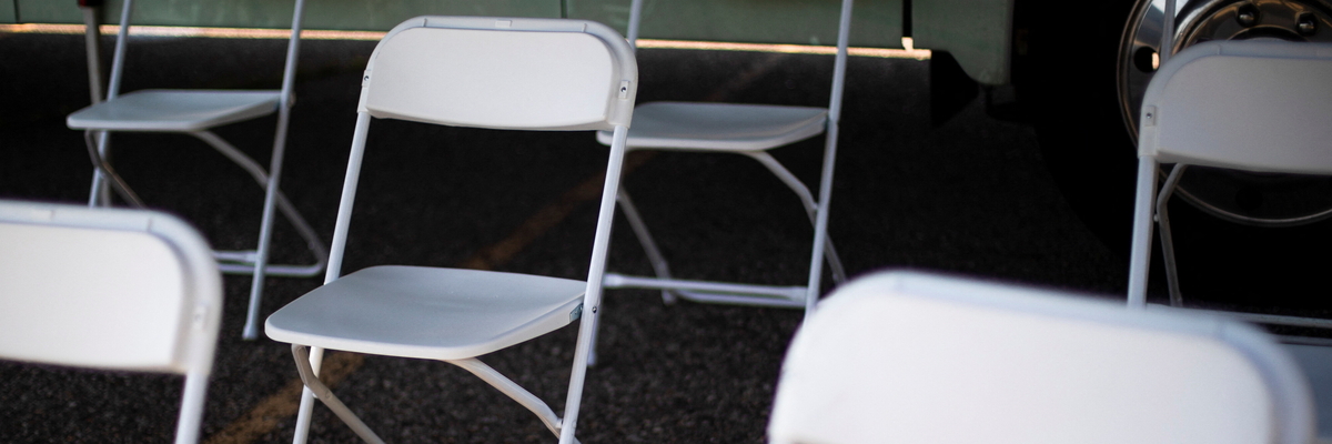 Leere weiße Klappstühle in einem Wartebereich. Ein Sonnenstrahl scheint auf den Fußboden.