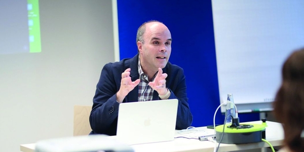 David Röthler sitzt an einem Tisch mit Laptop und erklärt etwas.