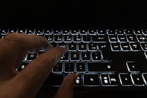 Finger tippen auf eine beleuchtete schwarze Tastatur.