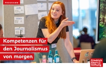 Foto einer jungen weiblich gelesenen Person vor einer Pinnwand, die Teilnehmenden etwas erklärt. Dazu steht in einem roten Balken mit weißer Schrift: Kompetenzen für den Journalismus von Morgen