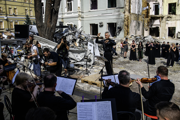 Ein Dirigent dirigiert ein Sinfonieorchester unter freiem Himmel vor den Ruinen einen Kinderkrankenhauses in Kiew. Das Haus ist von Bomben zerstört worden. 