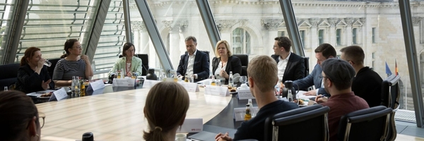 Die Teilnehmenden sitzen an einem Tisch im Bundestag und sind im Gespräch Nancy Faeser.