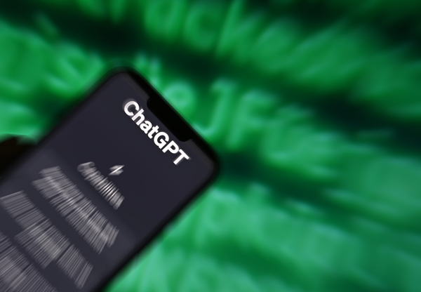 Ein Smartphone vor verschwommenem Hintergrund. Der Hintergrund zeigt grüne Buchstaben auf einem schwarzen Bildschirm. Das Smartphone hat ChatGPT geöffnet.