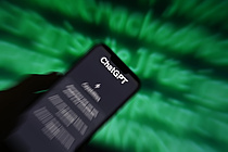 Ein Smartphone vor verschwommenem Hintergrund. Der Hintergrund zeigt grüne Buchstaben auf einem schwarzen Bildschirm. Das Smartphone hat ChatGPT geöffnet.