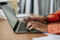 Die Hände einer jungen Businessfrau, die auf einem Schreibtisch einen Laptop bedient.