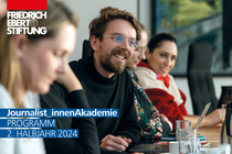 Titelbild des Jahresprogramms: Programm 2. Halbjahr 2024. Seminarteilnehmende sitzen an einem Tisch. Ein junger Mann ist im Fokus und lächelt aufmerksam. 