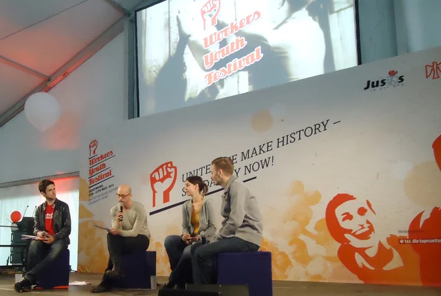 Jochen Steinhilber auf dem Worker's Youth Festival auf der Bühne. Er spricht in ein Mikrofon. 