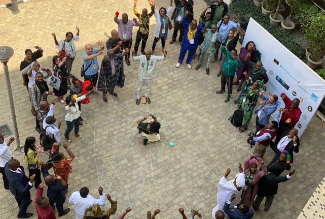 Teilnehmer:innen der Konferenz "LAUNCH OF CIVIL SOCIETY GFMD 2023 PROCESS" in Abuja/Nigeria halten Fäden in den Händen, die sich zu einem Netzwerk verbinden.