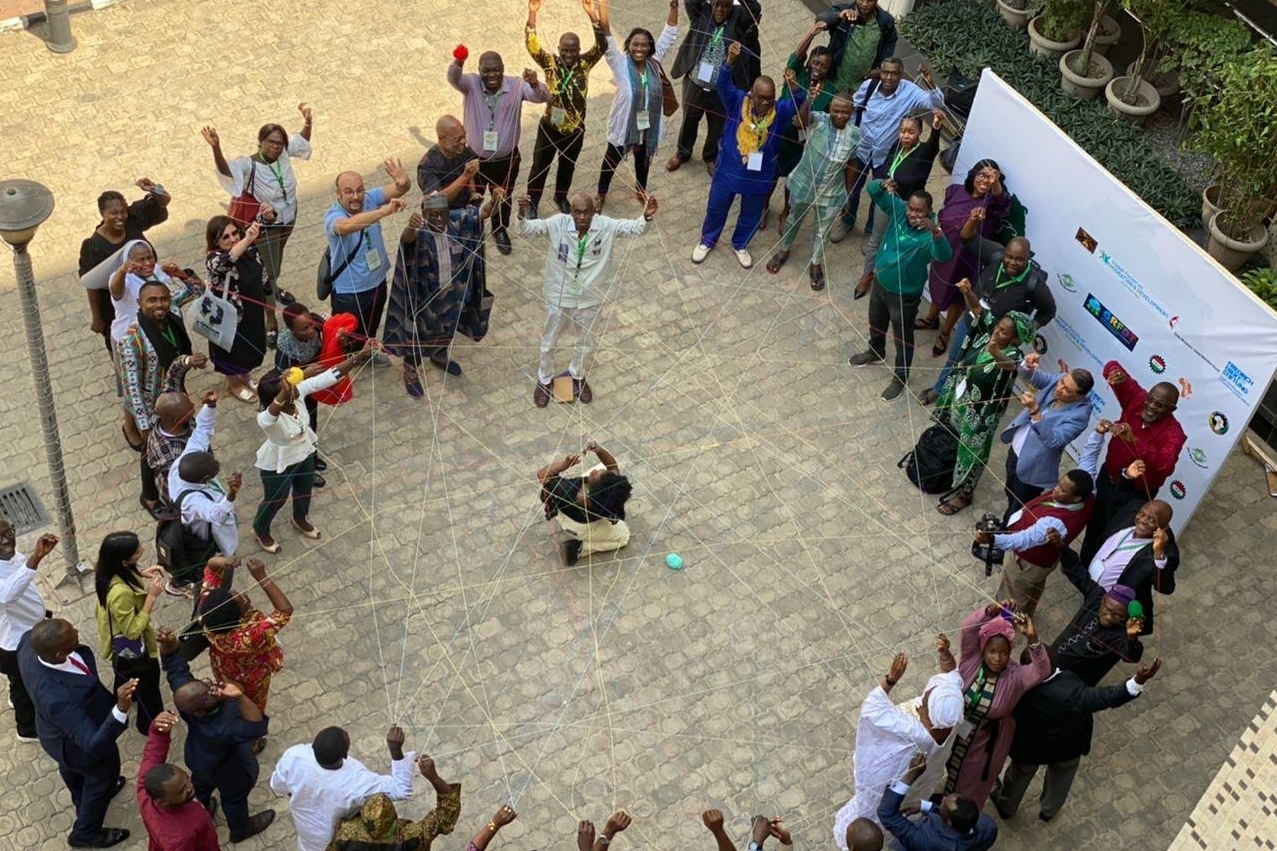 Teilnehmer:innen der Konferenz "LAUNCH OF CIVIL SOCIETY GFMD 2023 PROCESS" in Abuja/Nigeria halten Fäden in den Händen, die sich zu einem Netzwerk verbinden.