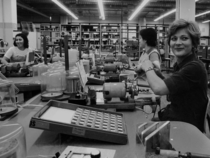 Die blonde Arbeiterin rechts im Vordergrund und die Arbeiterinnen im Hintergrund produziert Schaltschränke für Telefonnetze.