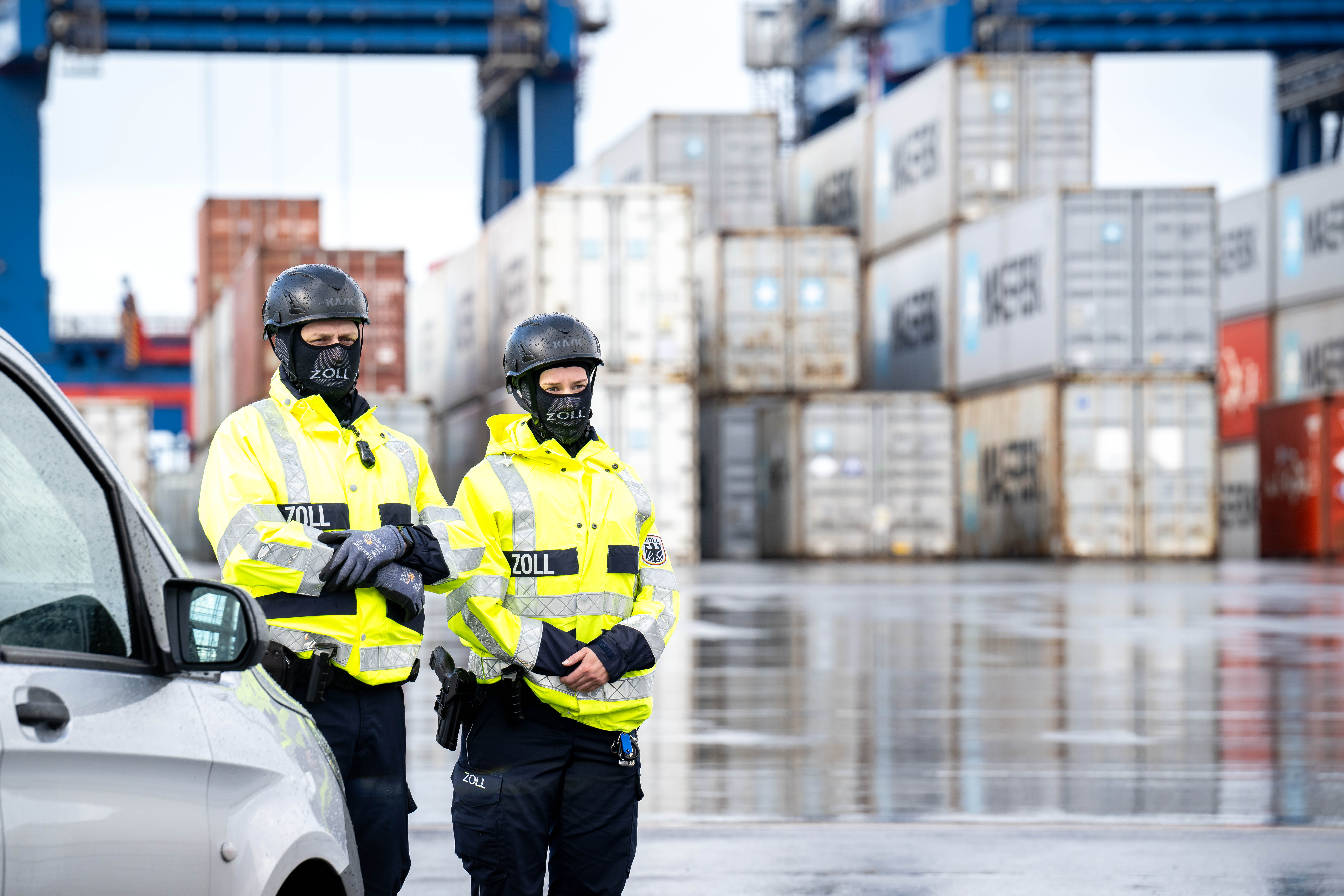 Zwei Polizist_innen stehen in einem Hafen vor Containern.